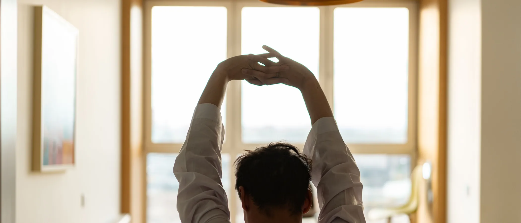 Person seen from behind stretching their arms overhead in front of a sunlit window