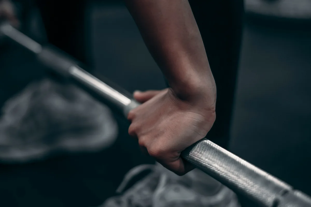Hand gripping a steel barbell in low light