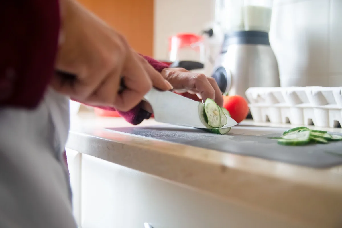 Hands slicing cucumber on a board in a home kitchen