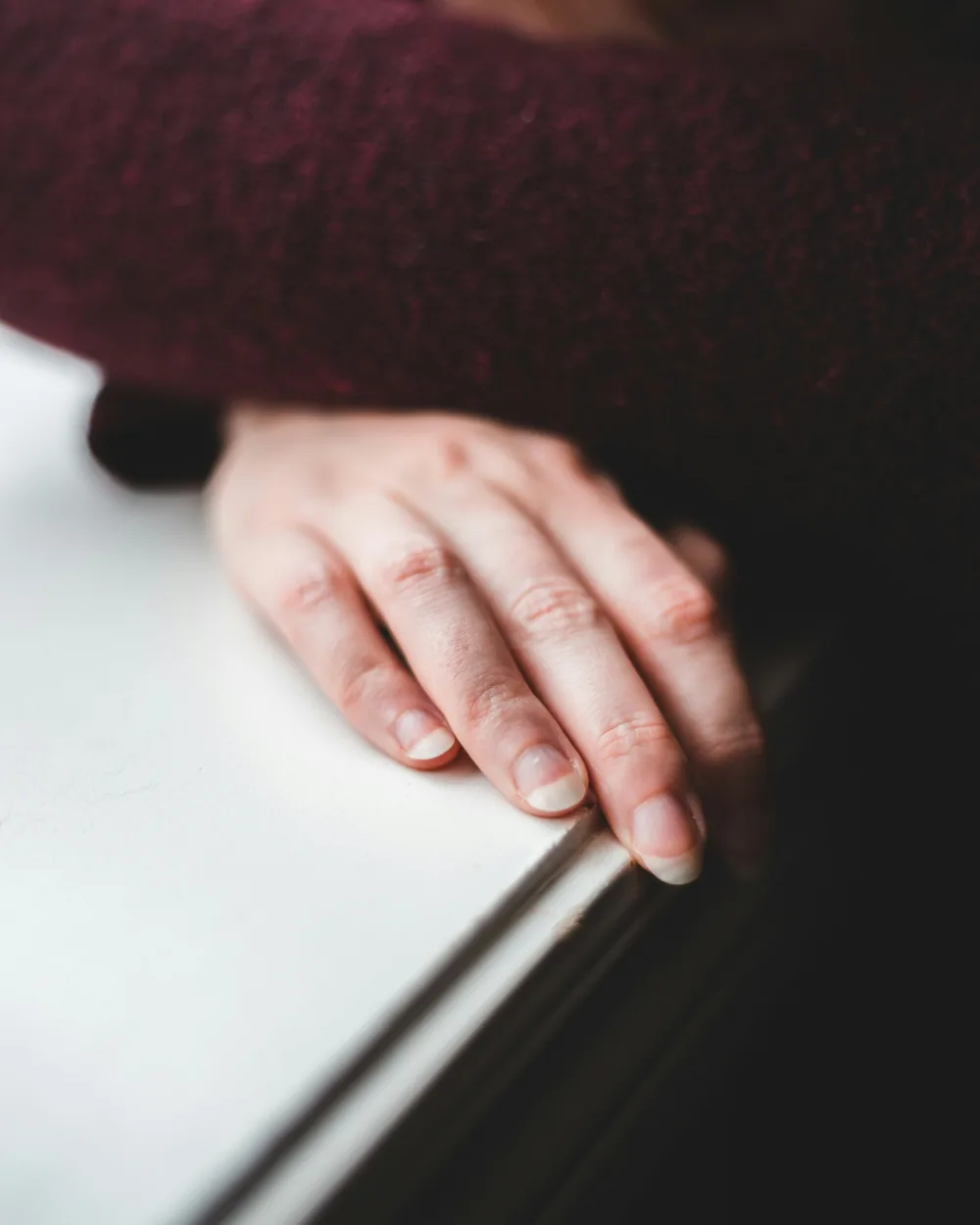 A hand resting on a window sill in soft daylight